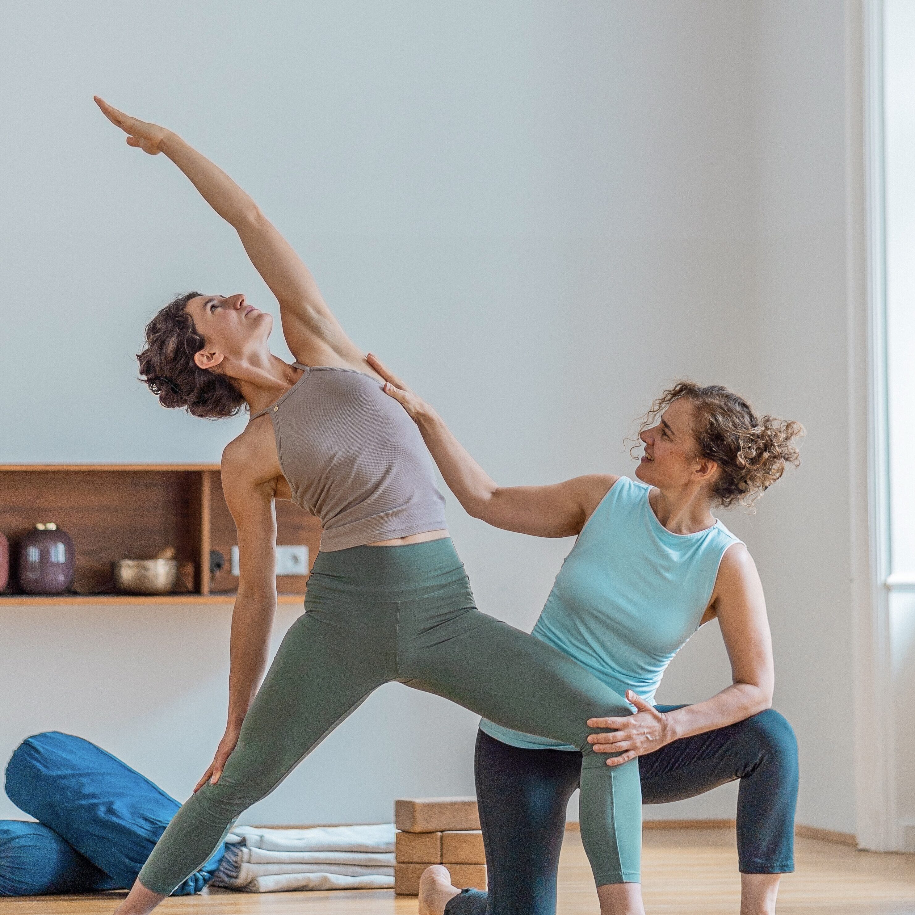 Yoga-Instruktor assistiert Schülerin bei einer Rückwärtsbeugeposition auf einer Yogamatte in einem hellen Trainingsraum